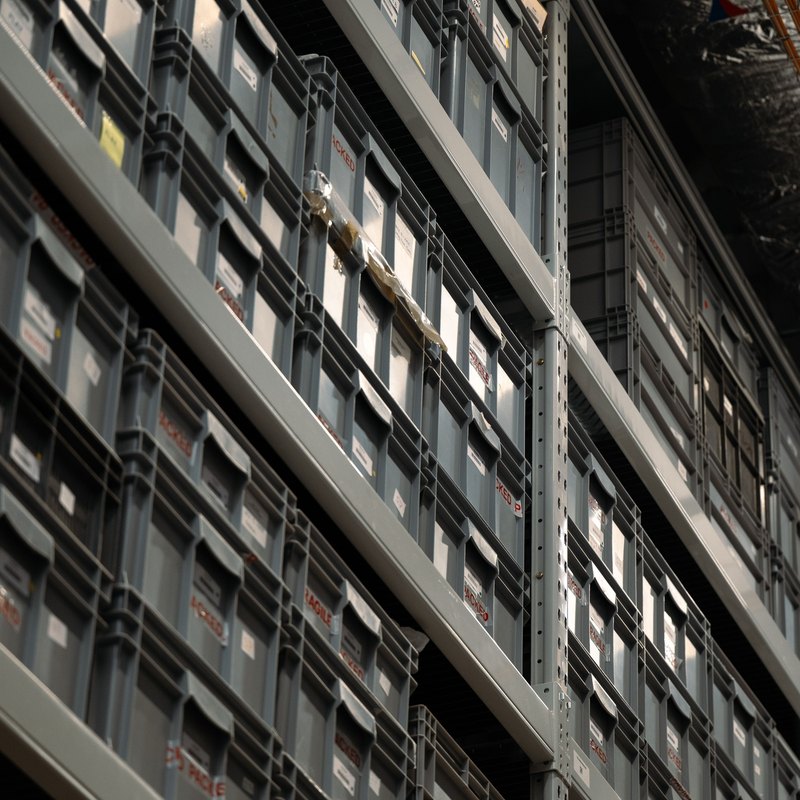 Gray plastic storage crates stacked on tall steel shelving in a warehouse