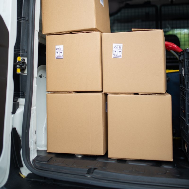 Taped cardboard boxes stacked inside the open back of a delivery van