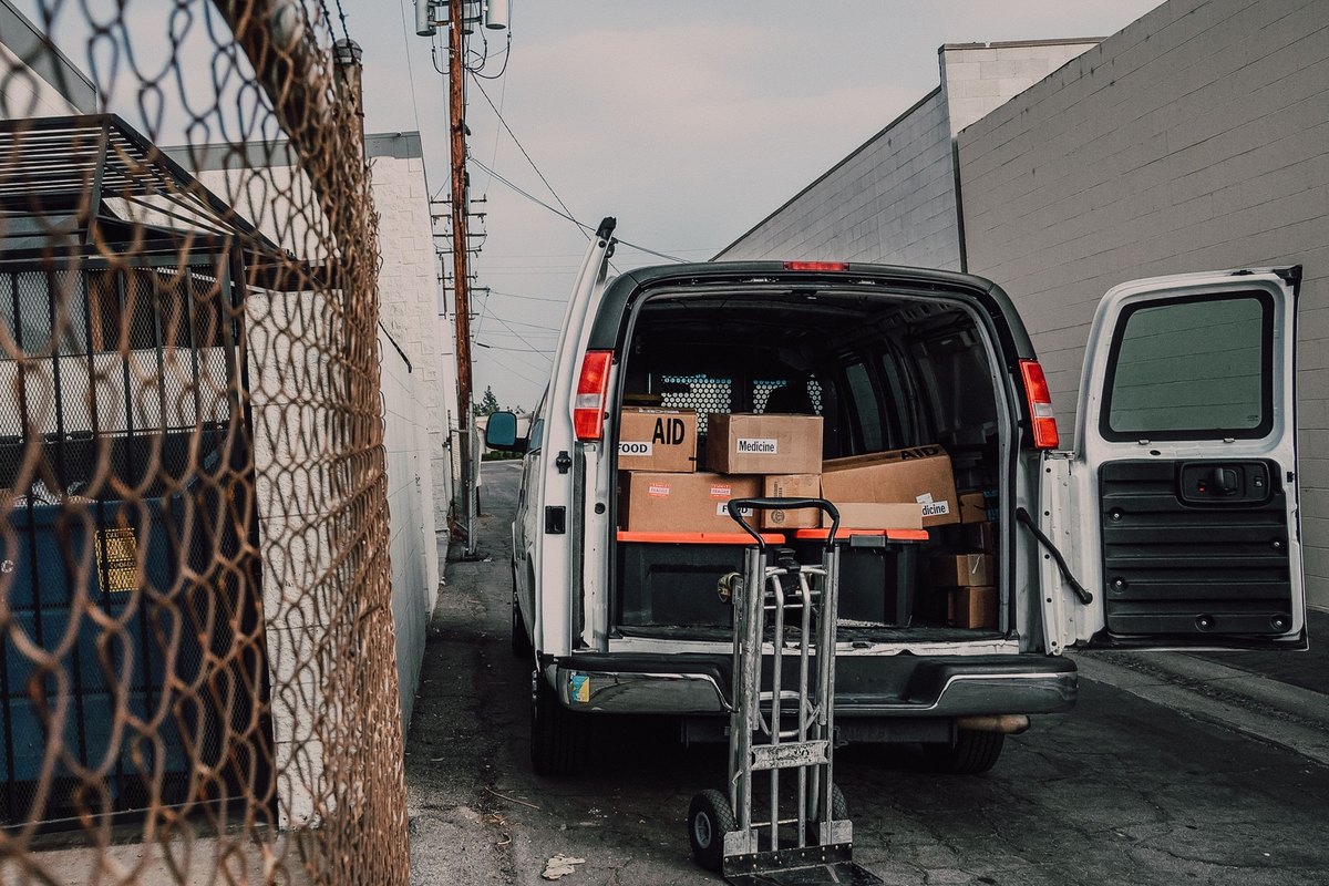 White cargo van with open doors and a hand trolley, loaded with cardboard boxes