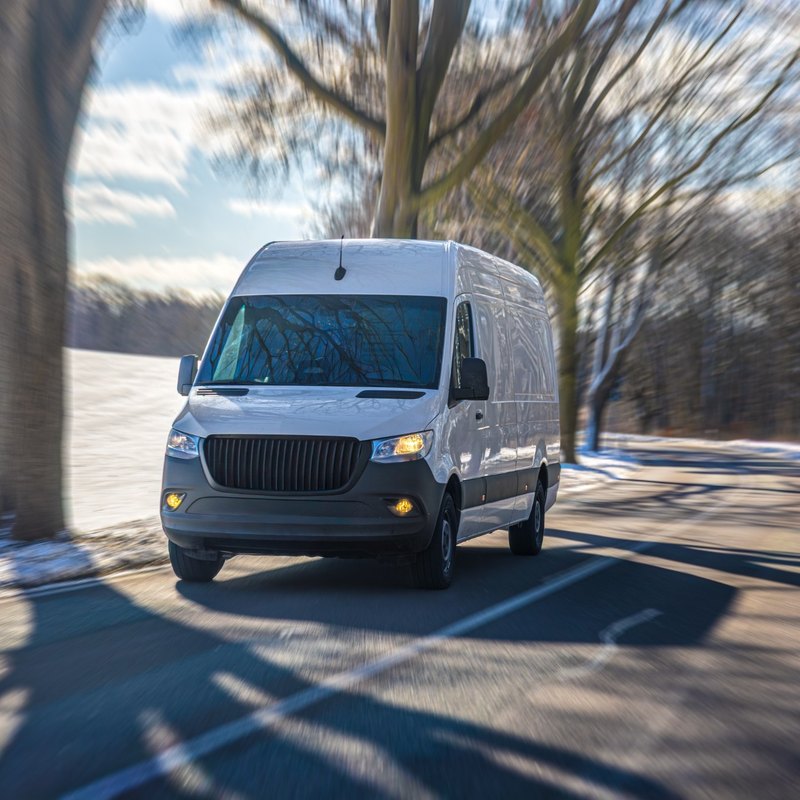 White delivery van driving down a tree-lined road