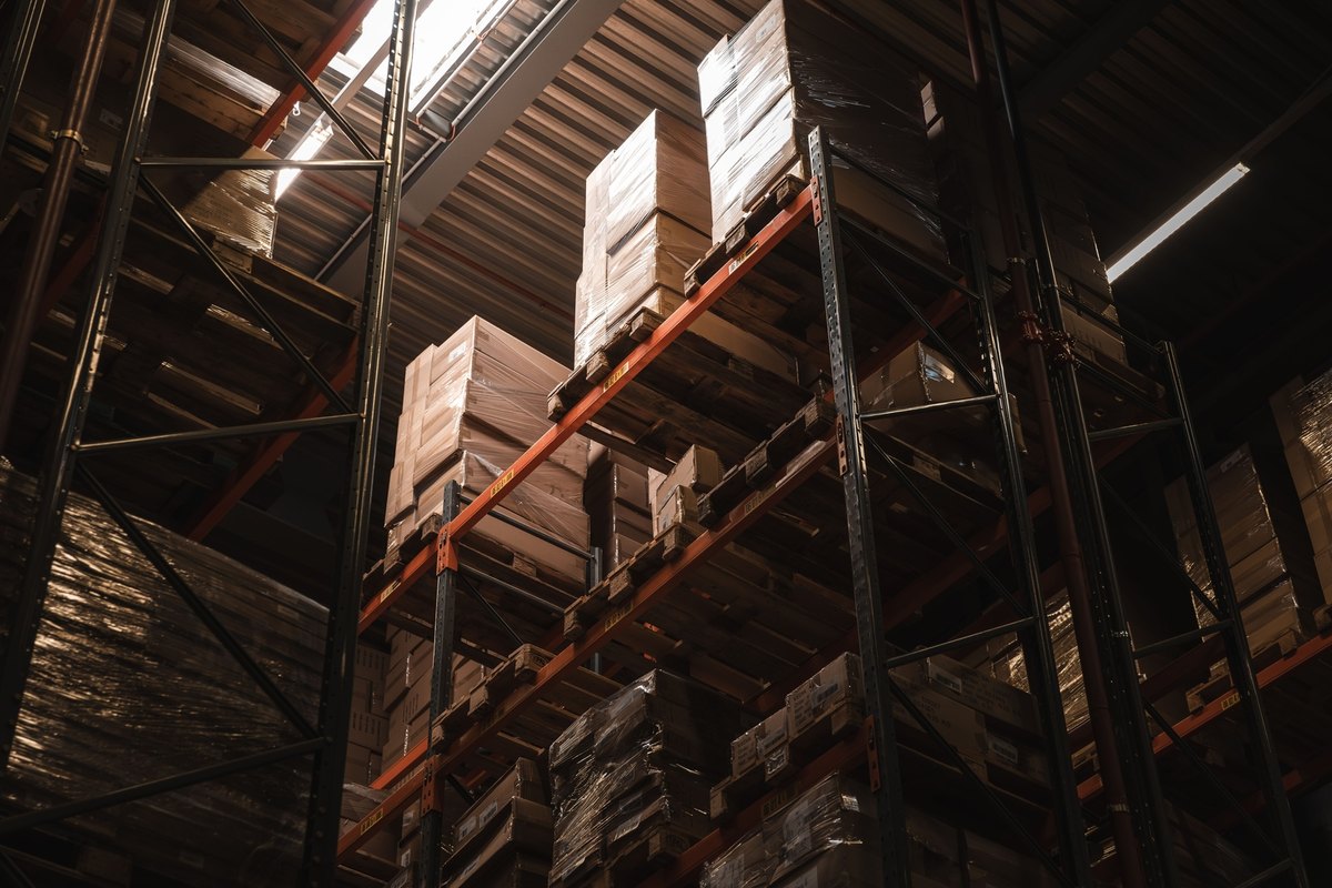 Tall steel pallet racks holding stacked cartons on wooden pallets in a warehouse interior