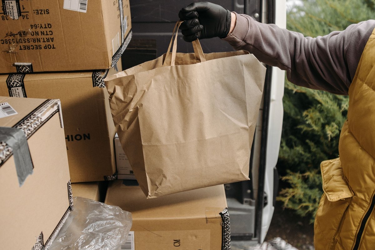 Gloved hand holding a paper bag at the open back of a van loaded with boxes