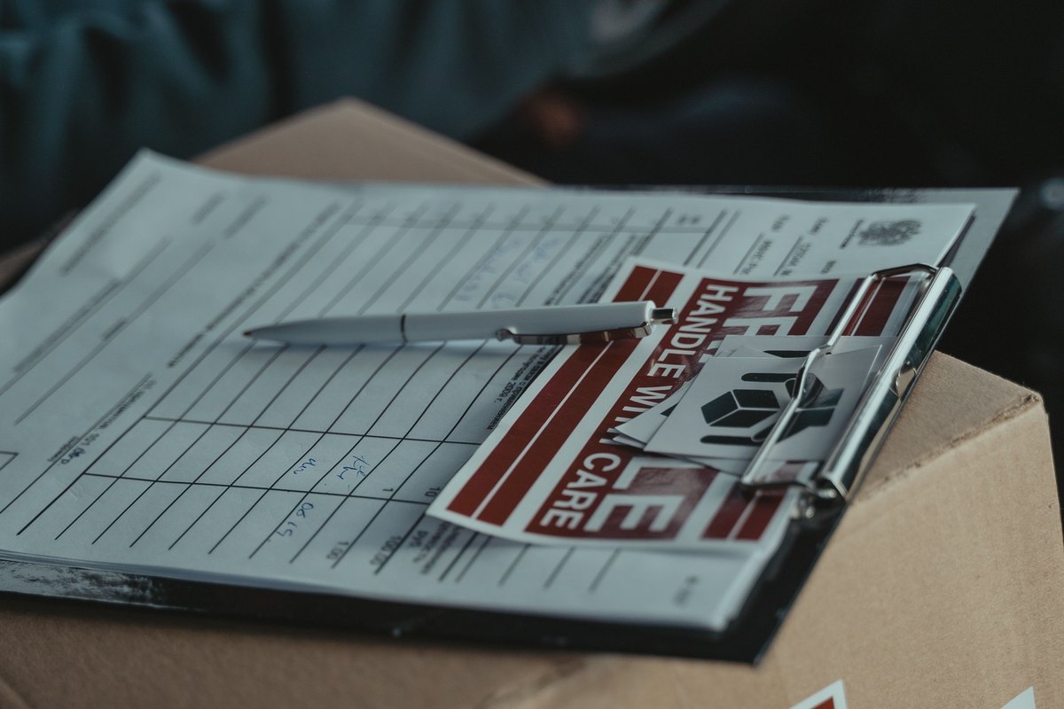 Delivery paperwork on a clipboard with a pen resting on a cardboard box