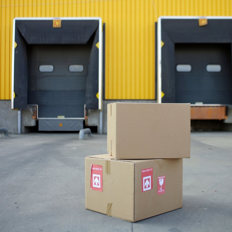 Open white delivery van loaded with stacked cardboard boxes and a crate of produce