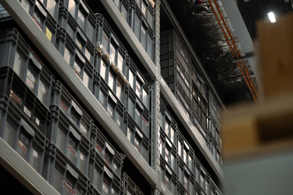 Gray plastic storage crates stacked on tall steel shelving in a warehouse