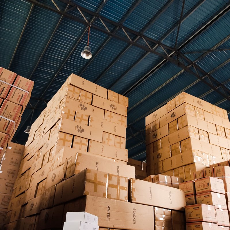 Tall stacks of cardboard boxes under the steel roof of a large warehouse